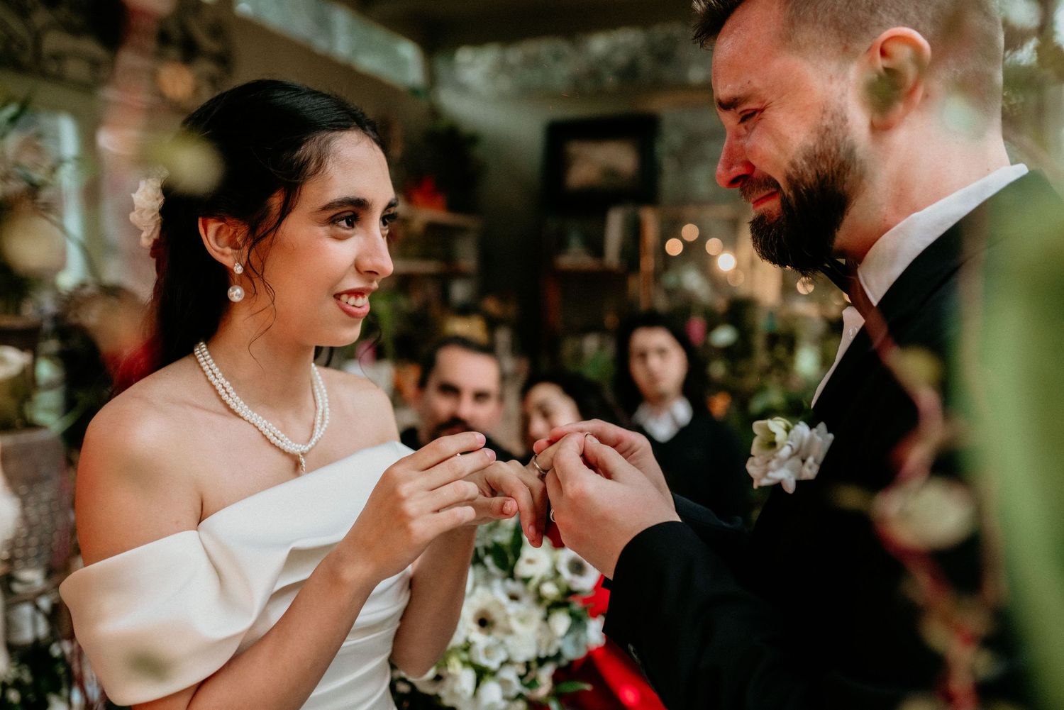 Two people sharing an intimate moment during ring exchange at indoor wedding ceremony with soft lighting and floral decor.