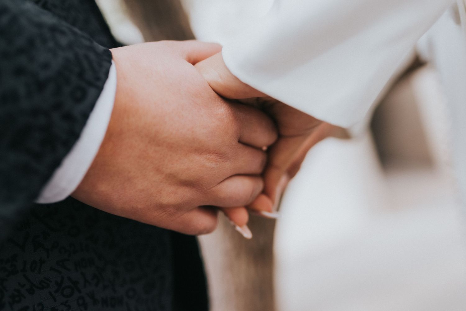 Close up of two hands wearing wedding bands touching tenderly in a romantic embrace.