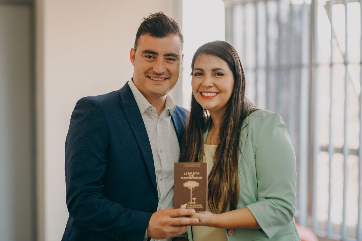 Happy couple posing together while holding a brown book in a home setting.