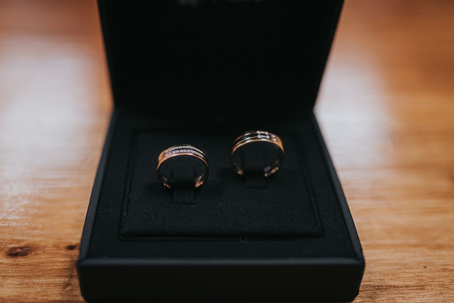A close-up view of two gold wedding rings resting on a black velvet jewelry box surface in warm lighting.
