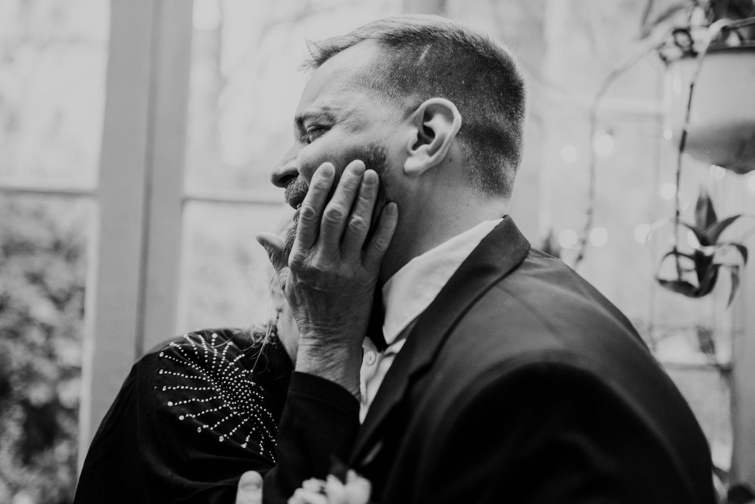 Black and white photo of three stylishly dressed groomsmen having a drink while laughing together outdoors.