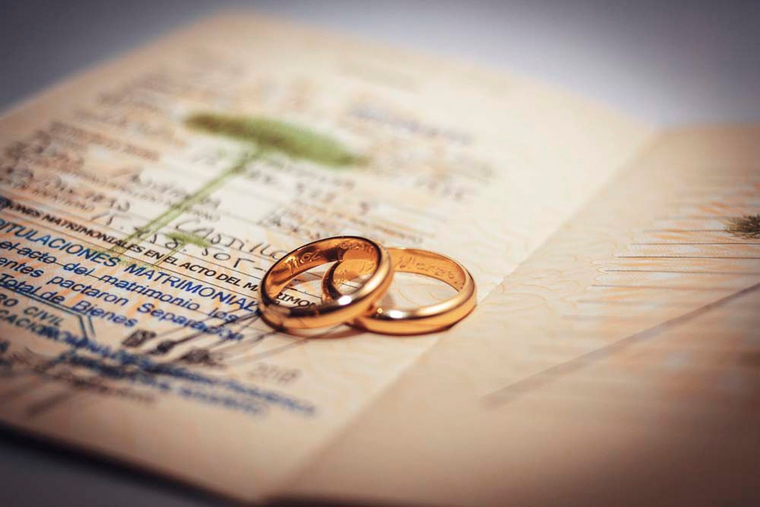 Two gold wedding rings rest on a vintage document with blurred text in soft focus.
