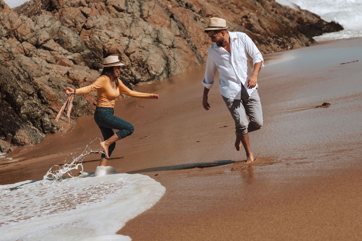 Couple walking on sandy beach near rocky coastal cliffs during daytime.