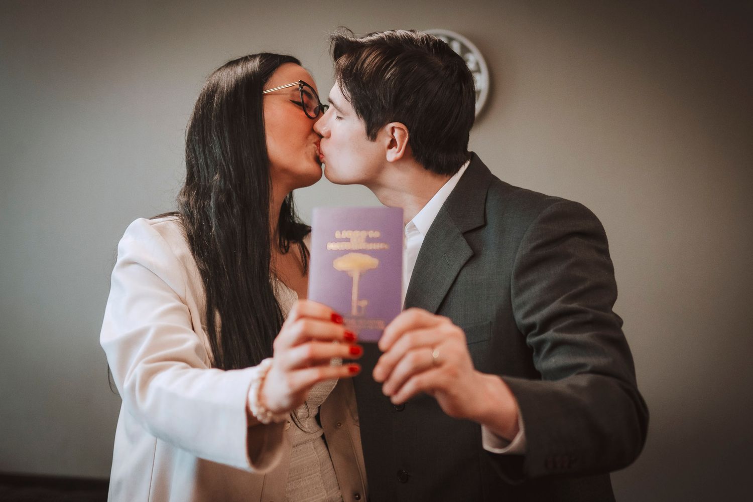Two people share a kiss while holding a purple passport book between them in a romantic moment.