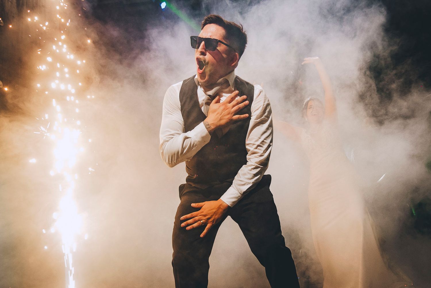 Dancing couple embracing in a misty venue with twinkling lights in the background.