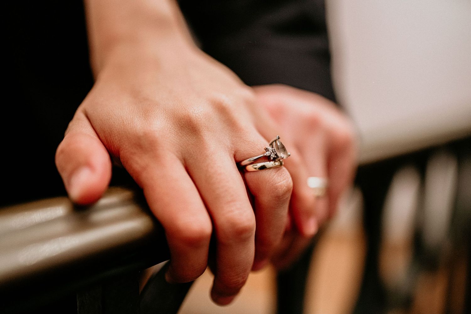 Close-up view of a hand wearing an elegant diamond engagement ring against a dark background.