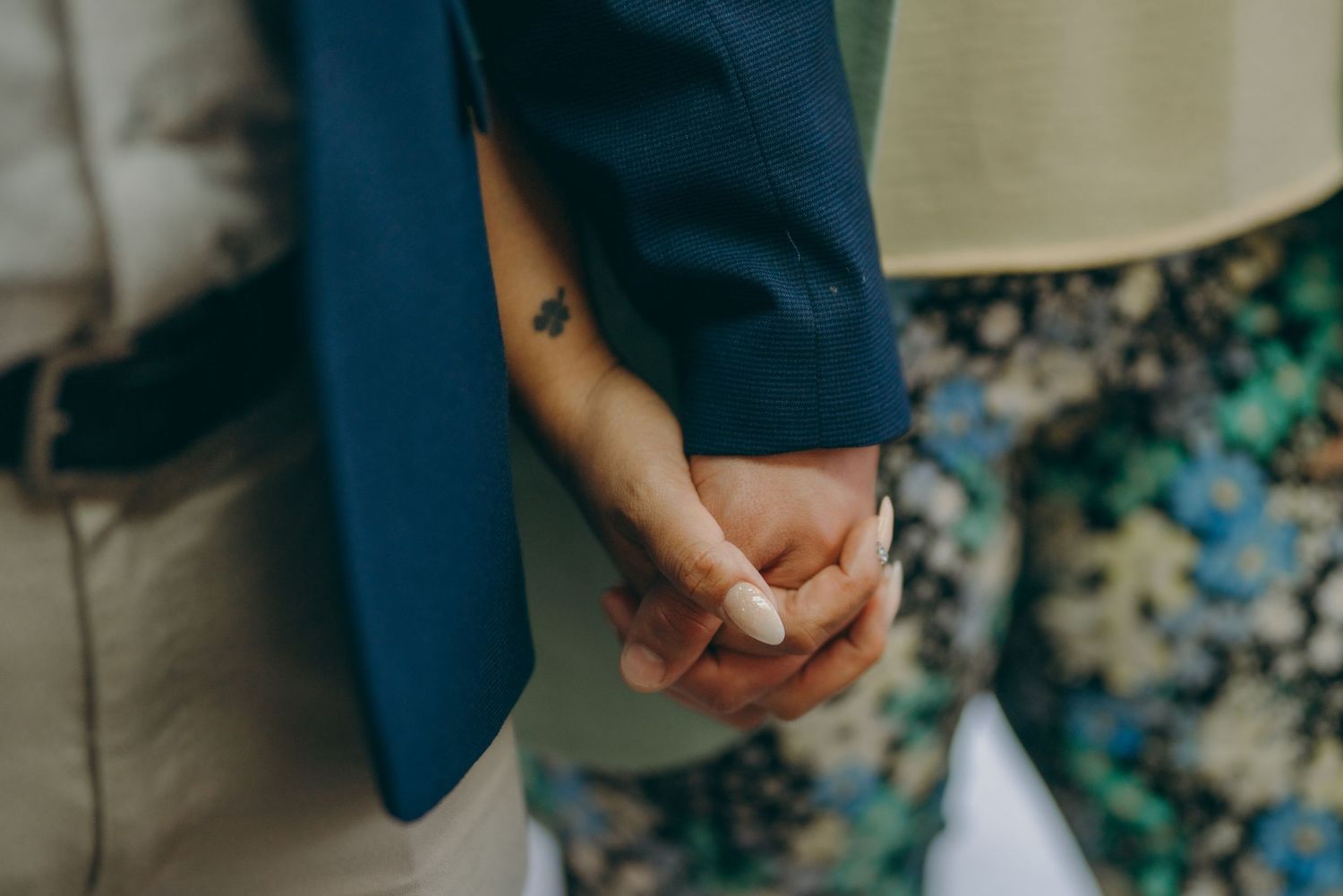 Close-up view of newlyweds holding hands in an outdoor garden setting against a floral backdrop.