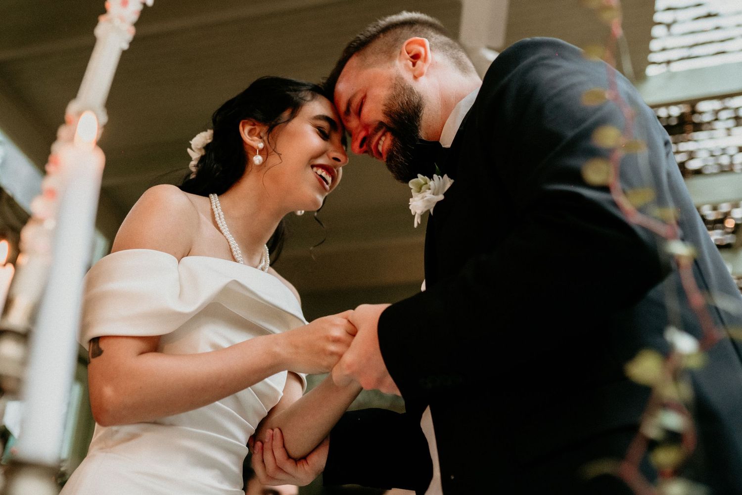 A laughing couple shares an intimate moment during their outdoor wedding celebration in natural sunlight.