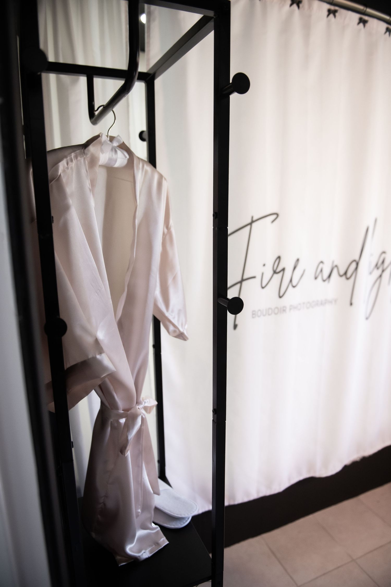 Complimentary client robe and slippers hangs on black metal clothing rack against white wall with handwritten text visible.