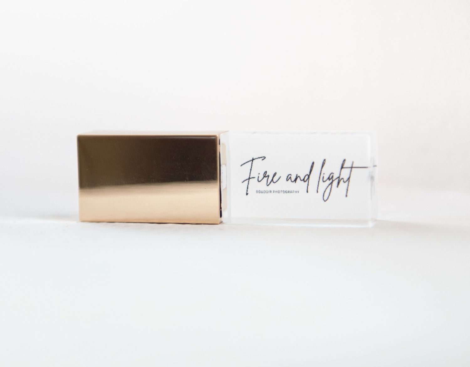 A gold metallic and clear USB drive with text reading 'Fire and light' on white surface with minimalist styling.