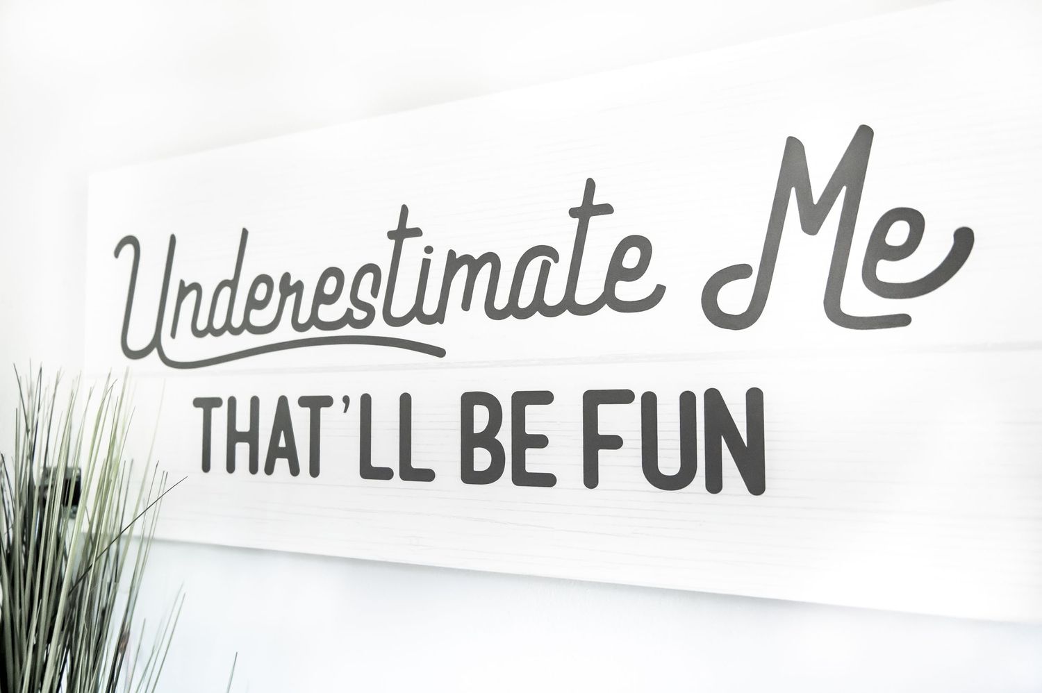'Underestimate me that'll be fun' sign on white wall.