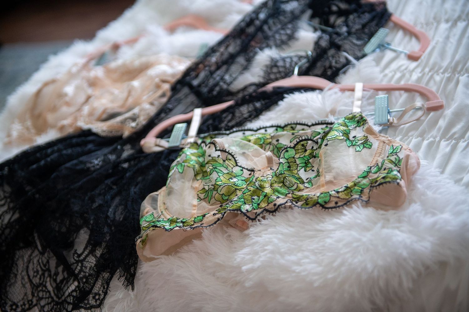 Close-up of delicate lingerie adorned with green beaded floral decorations resting on lace fabric.