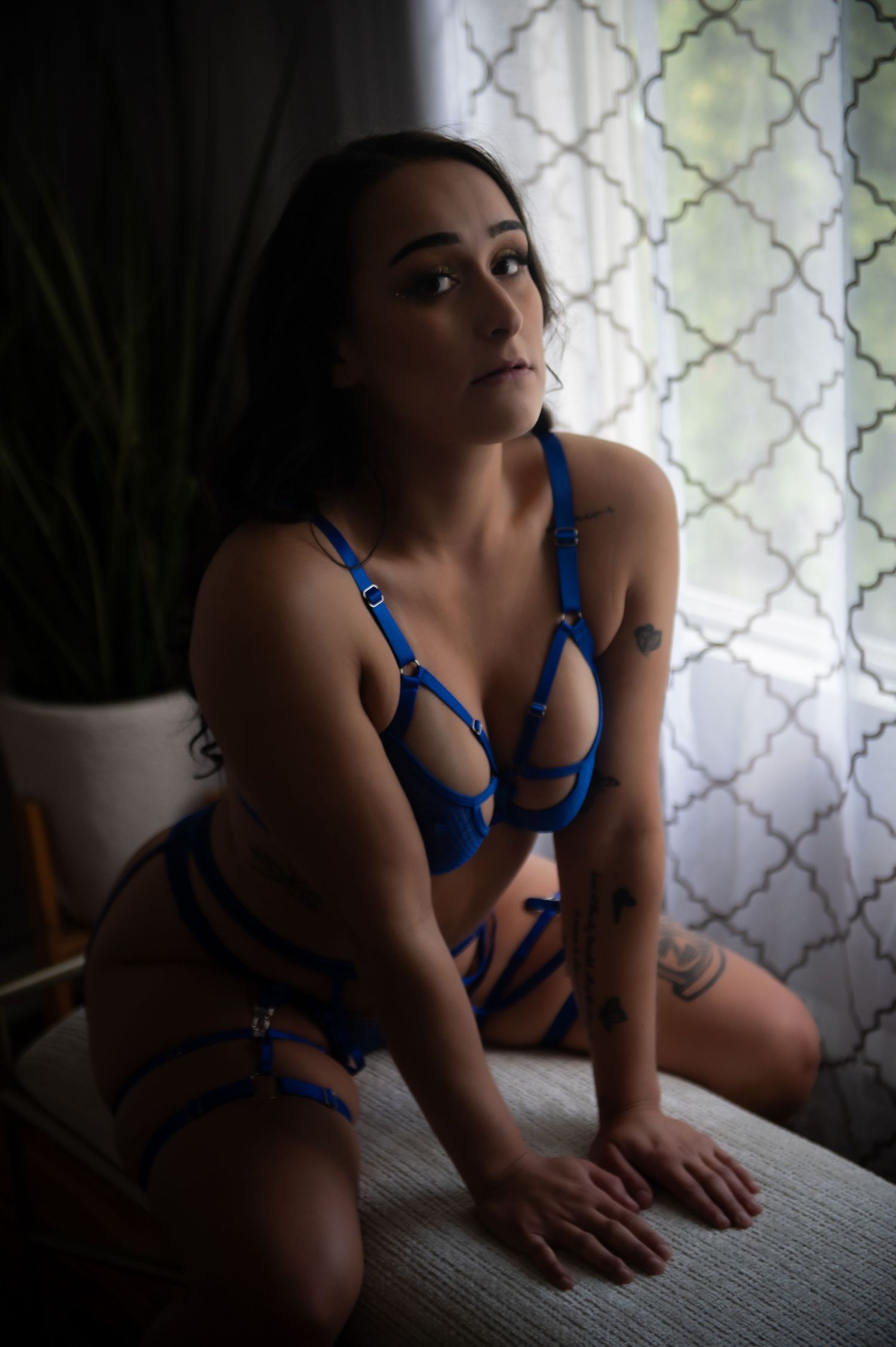 Intimate portrait by window with blue strappy lingerie and geometric curtain pattern.