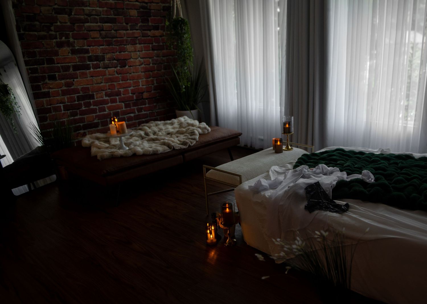 Sunlight streams through sheer curtains in a dark moody boudoir set with exposed brick walls and luxury bedding.