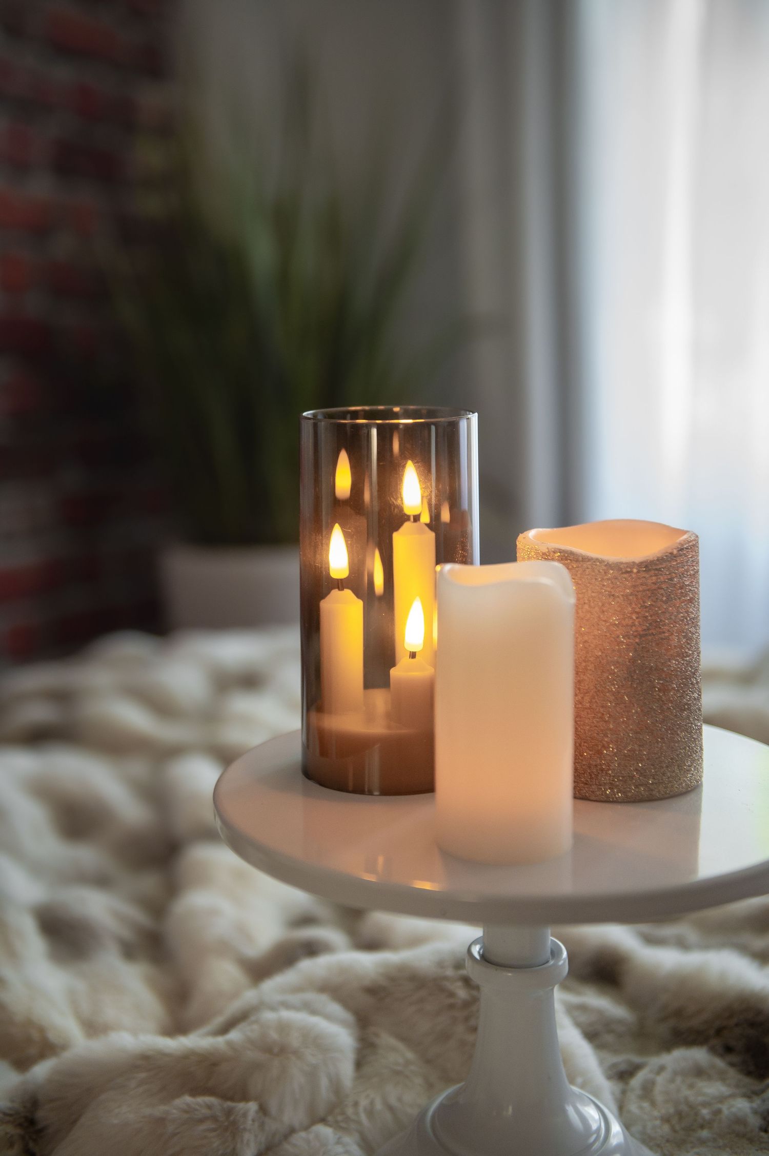 Lit candles arranged on a white ceramic cake stand create a cozy ambiance against a soft textured background.