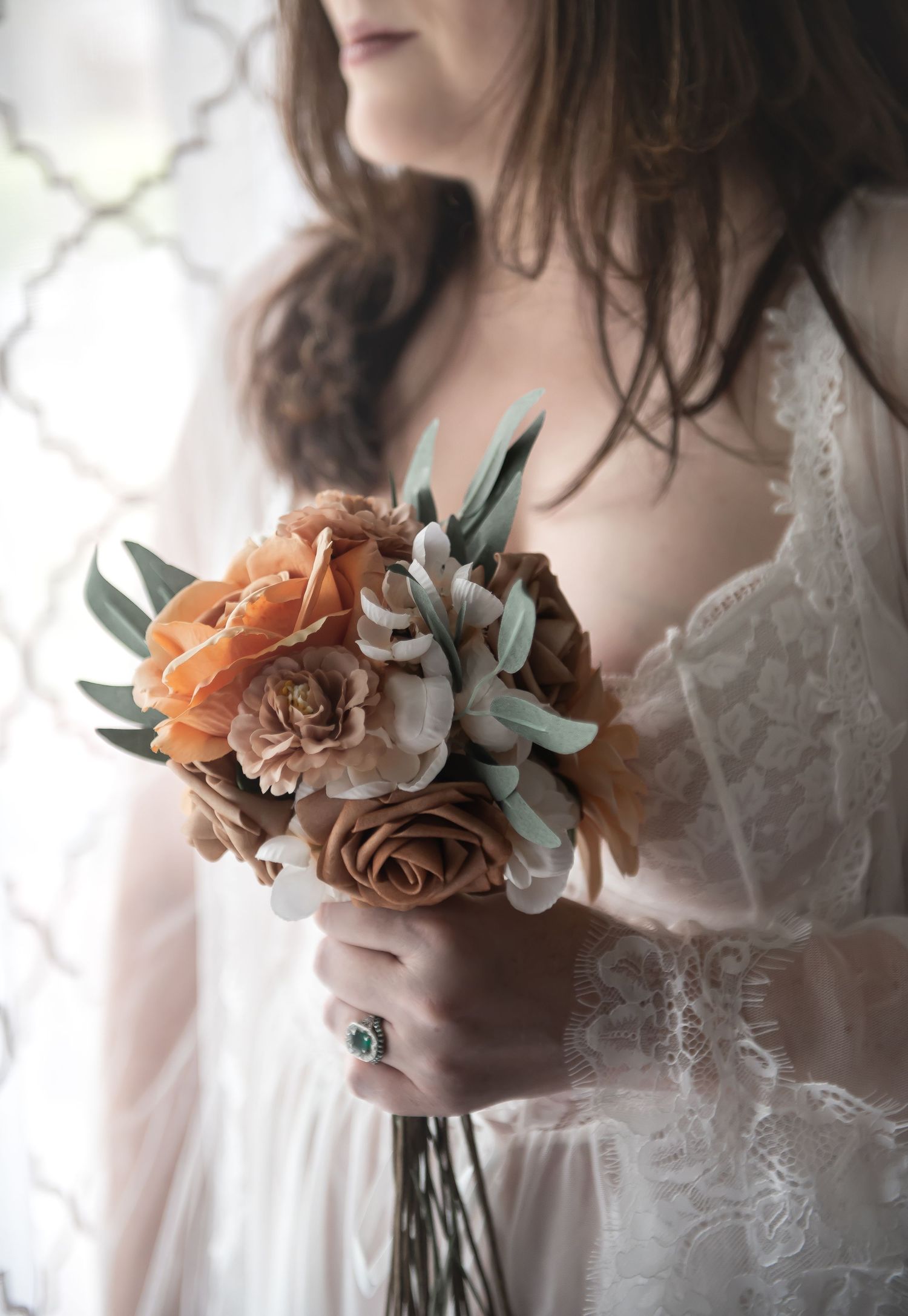 A soft, romantic bridal bouquet with peach roses and eucalyptus leaves held against a white lace dress.