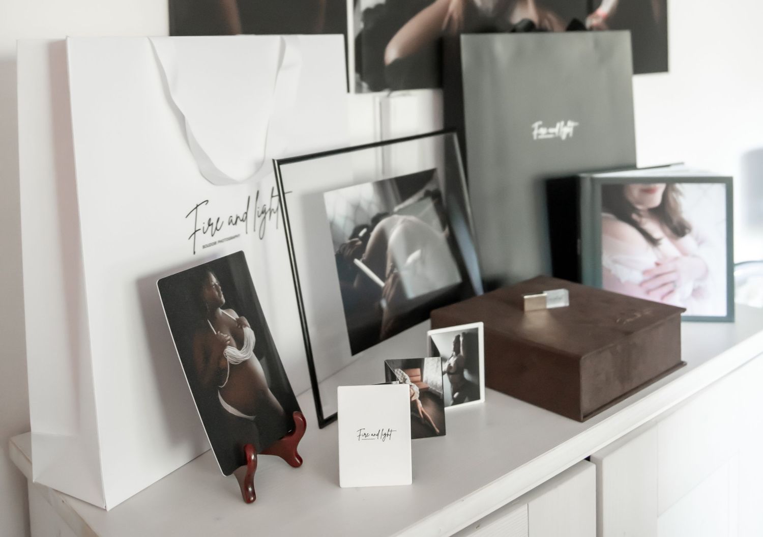 Professional photography branding display with black and white prints, shopping bags, and wooden boxes arranged on white shelf.