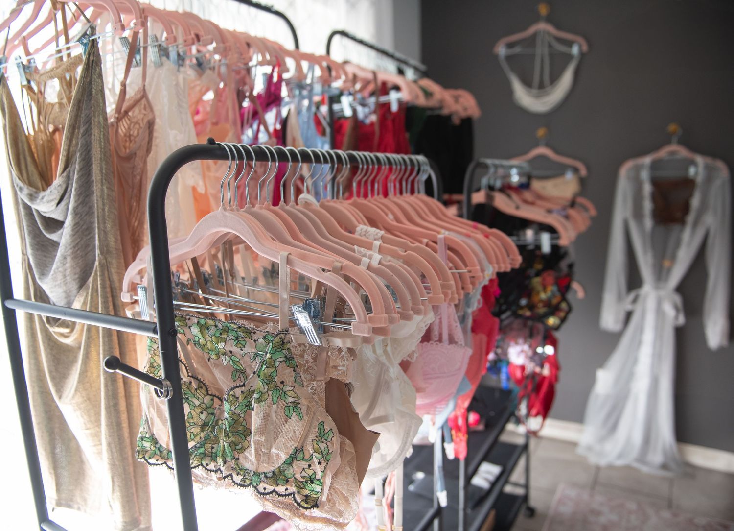 Clothing rack displays pink and neutral colored garments with hangers against a gray wall in boudoir client closet.