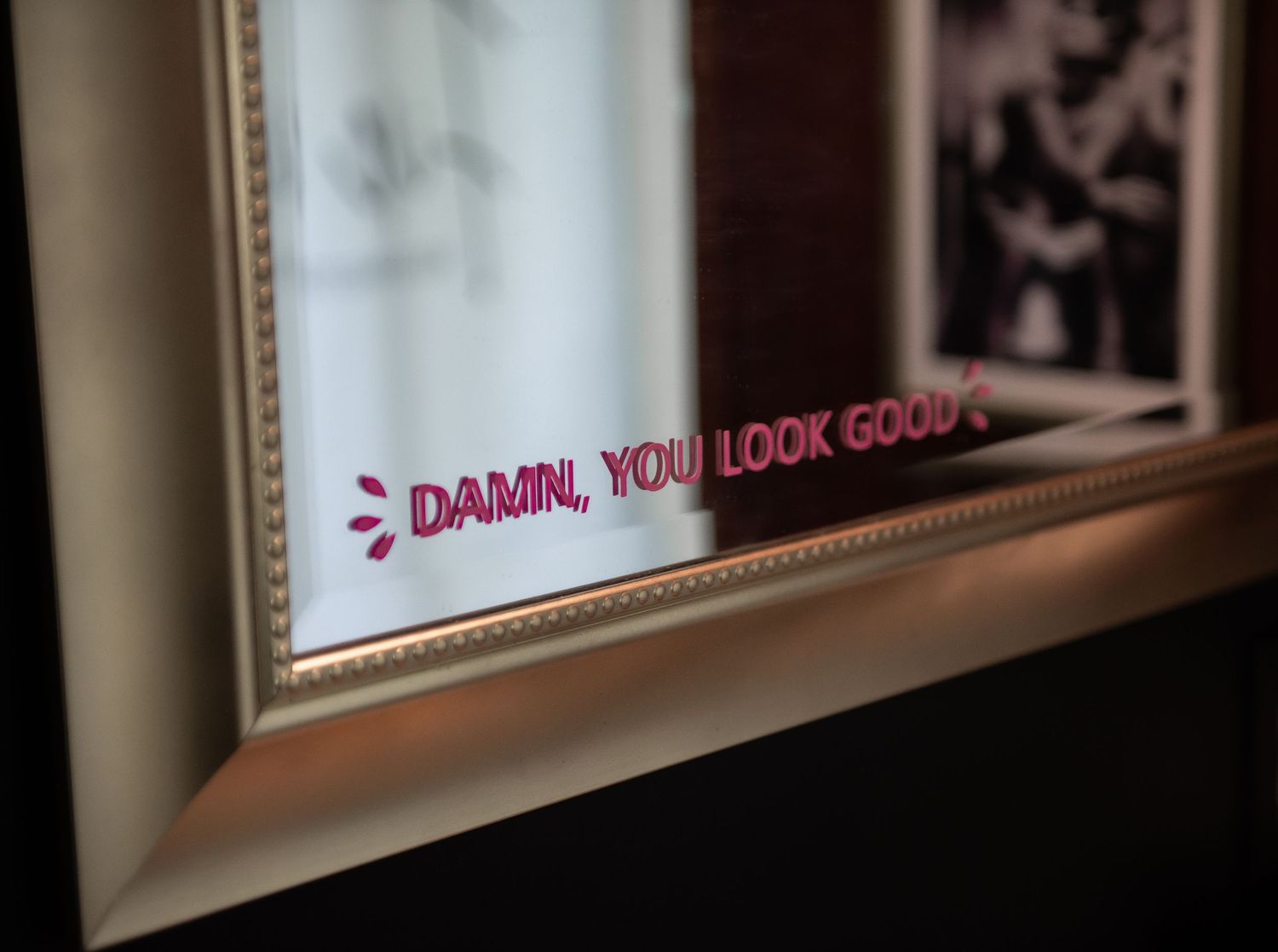 A framed gold boudoir bathroom mirror with pink text visible on its surface.