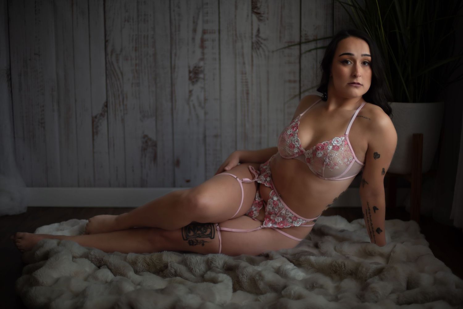Boudoir photo shoot on white fur with pink lingerie in moody lighting and rustic wood backdrop.