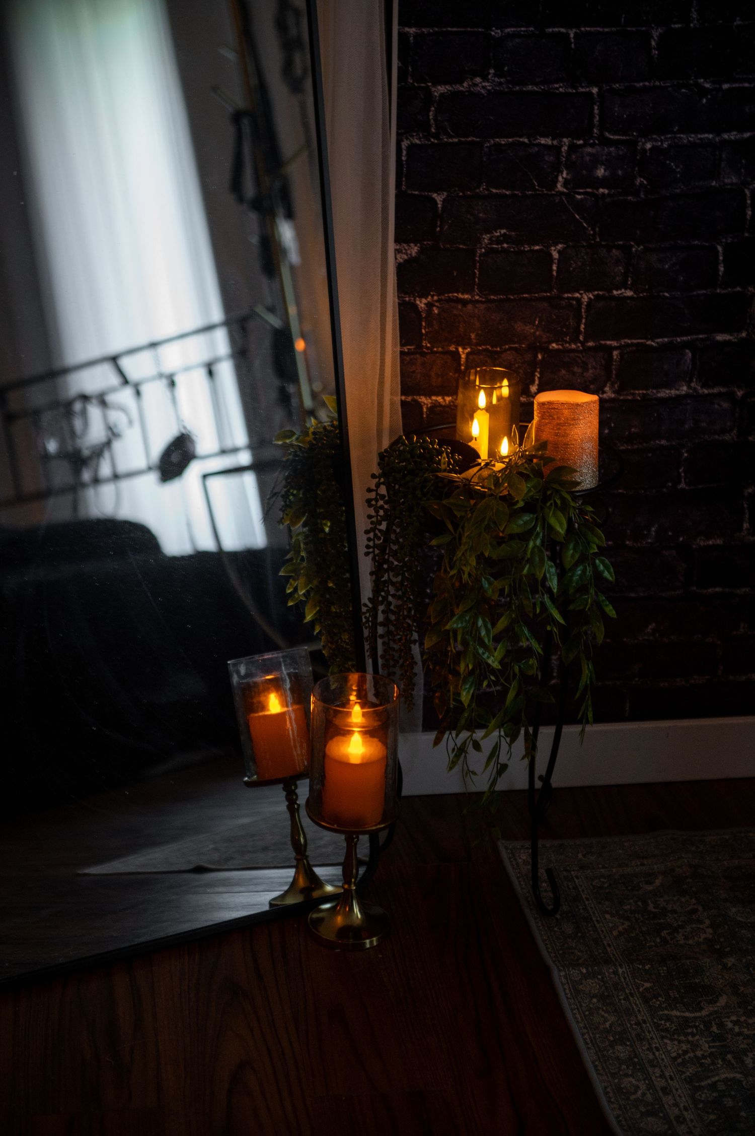 Candlelit boudoir set decorated with plants and candles creates a cozy, moody atmosphere against dark brick wall at night.