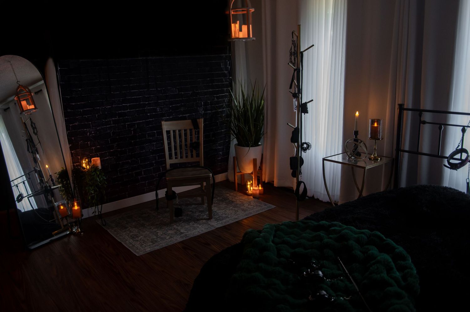 dark and moody room interior with candlelight, emerald green blanket, wooden chair, and dark brick fireplace at night.
