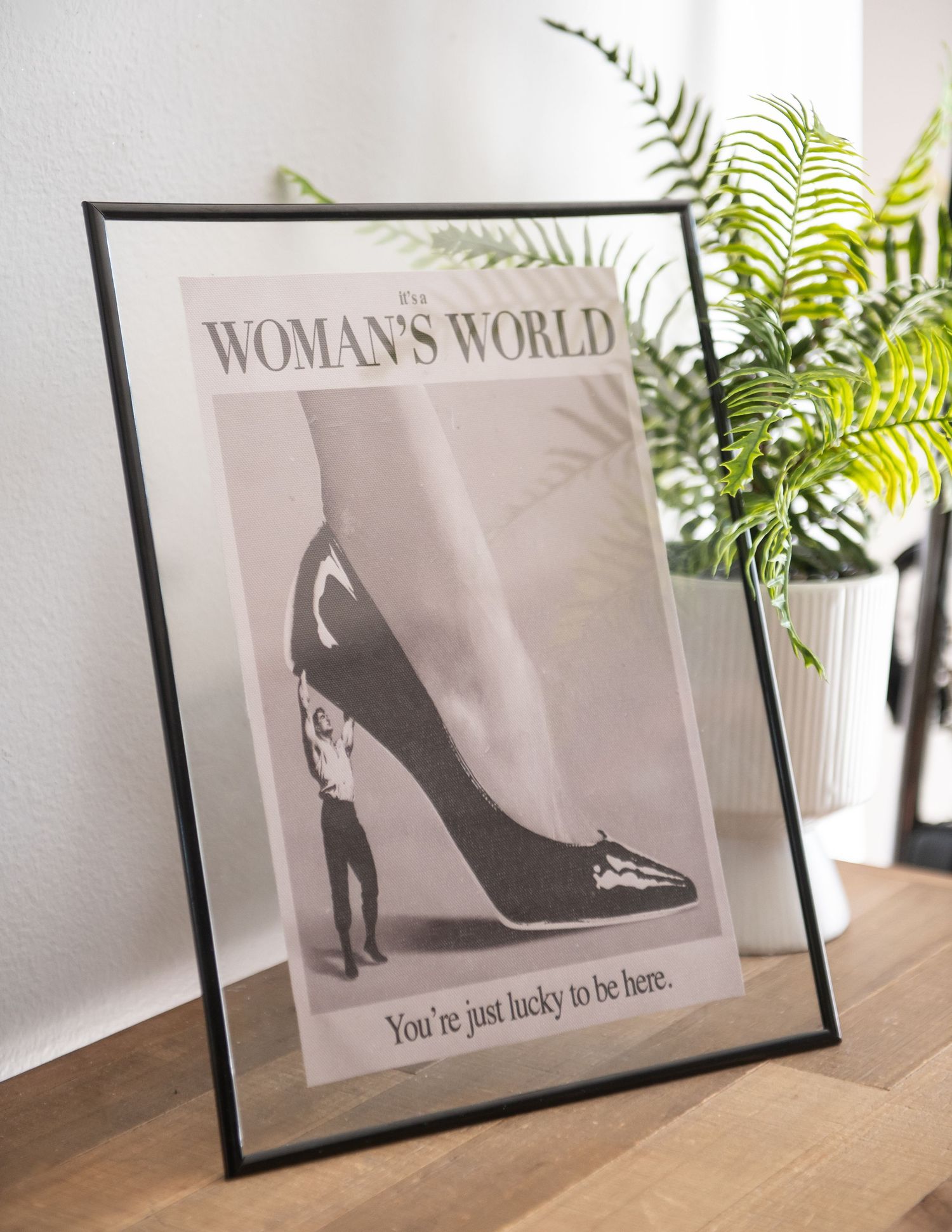 Framed vintage women empowerment black and white framed art print on shelf with green fern plants as decorative accents.