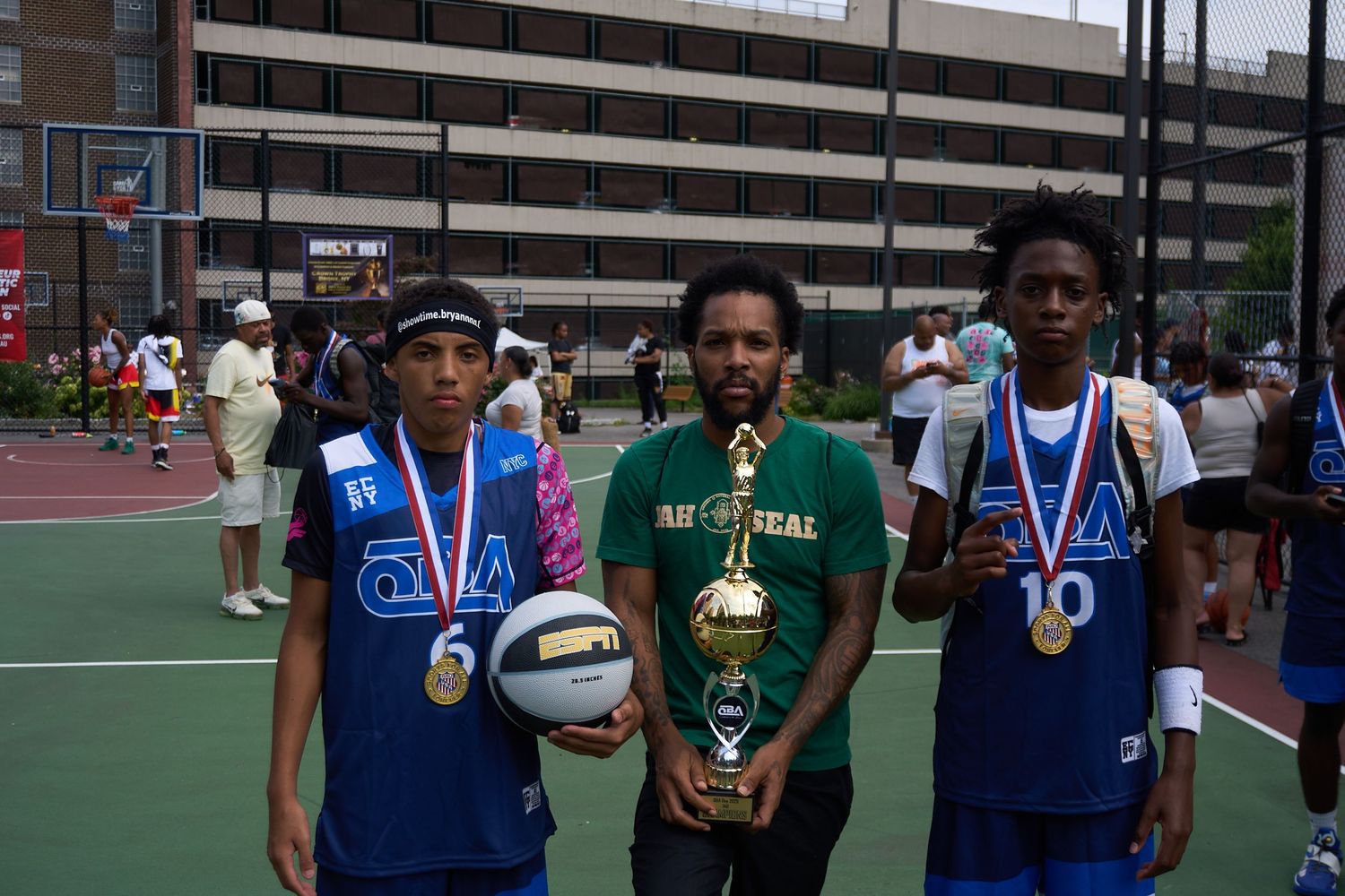 Three athletes stand together on a basketball court displaying their medals and trophies after a competition.