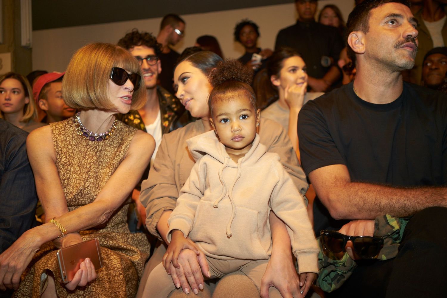 Audience members watch intently at an event with focused expressions while sitting in rows of seating.
