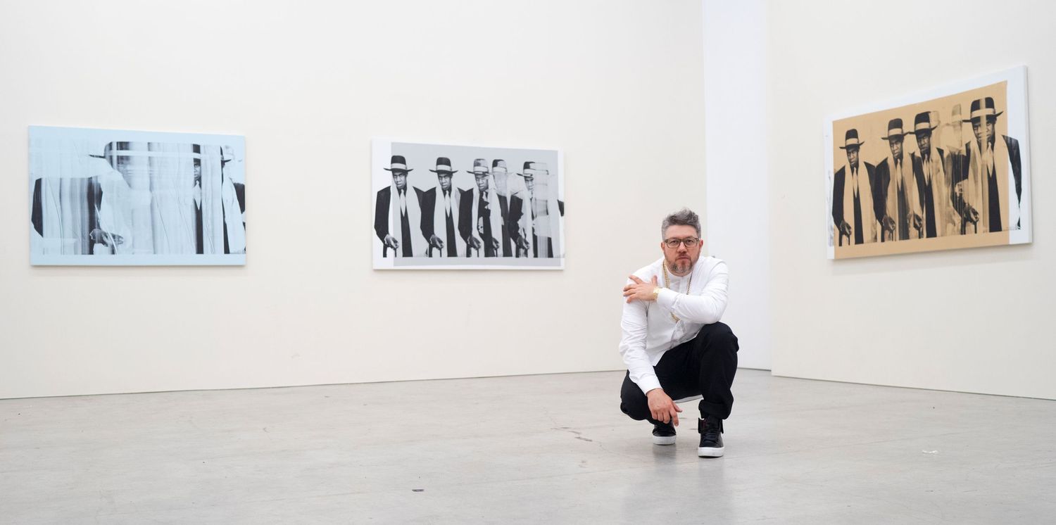 Gallery visitor crouches to view black and white photographic prints displayed in minimalist white exhibition space.