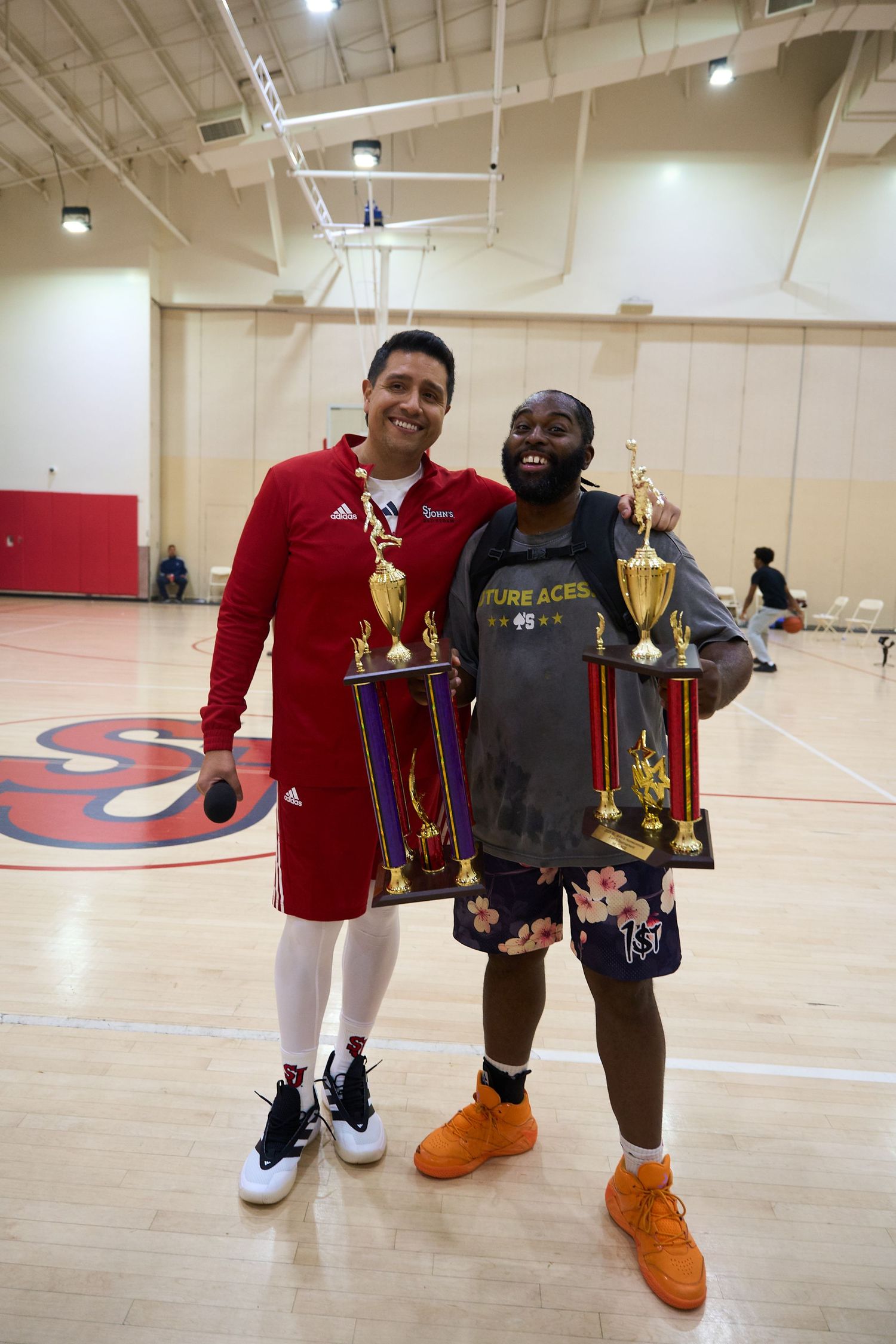 Winners displaying golden trophies on basketball court with red walls.