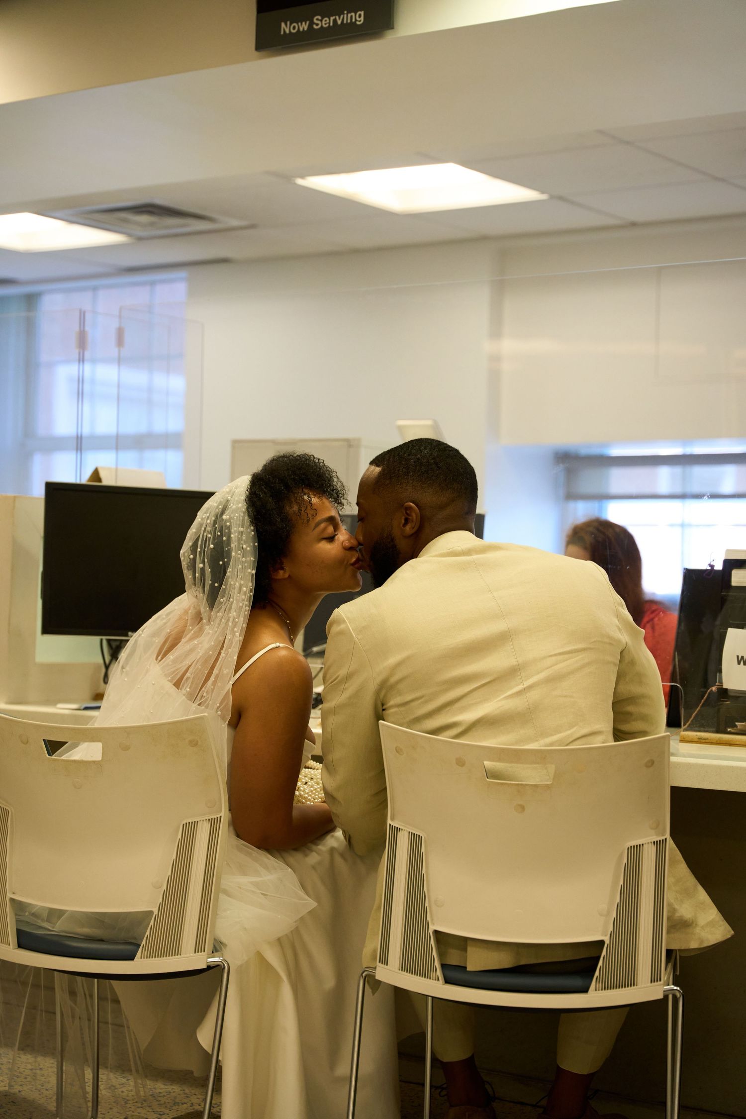 A couple in wedding attire share an intimate moment while seated at desks in an office setting.