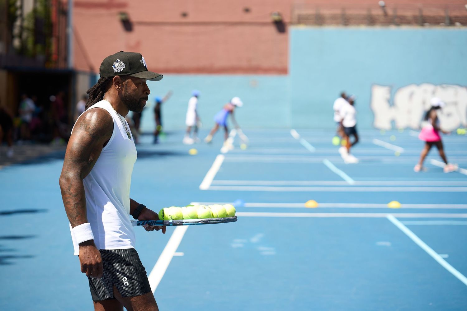 Tennis players practicing on bright blue courts with yellow training cones.