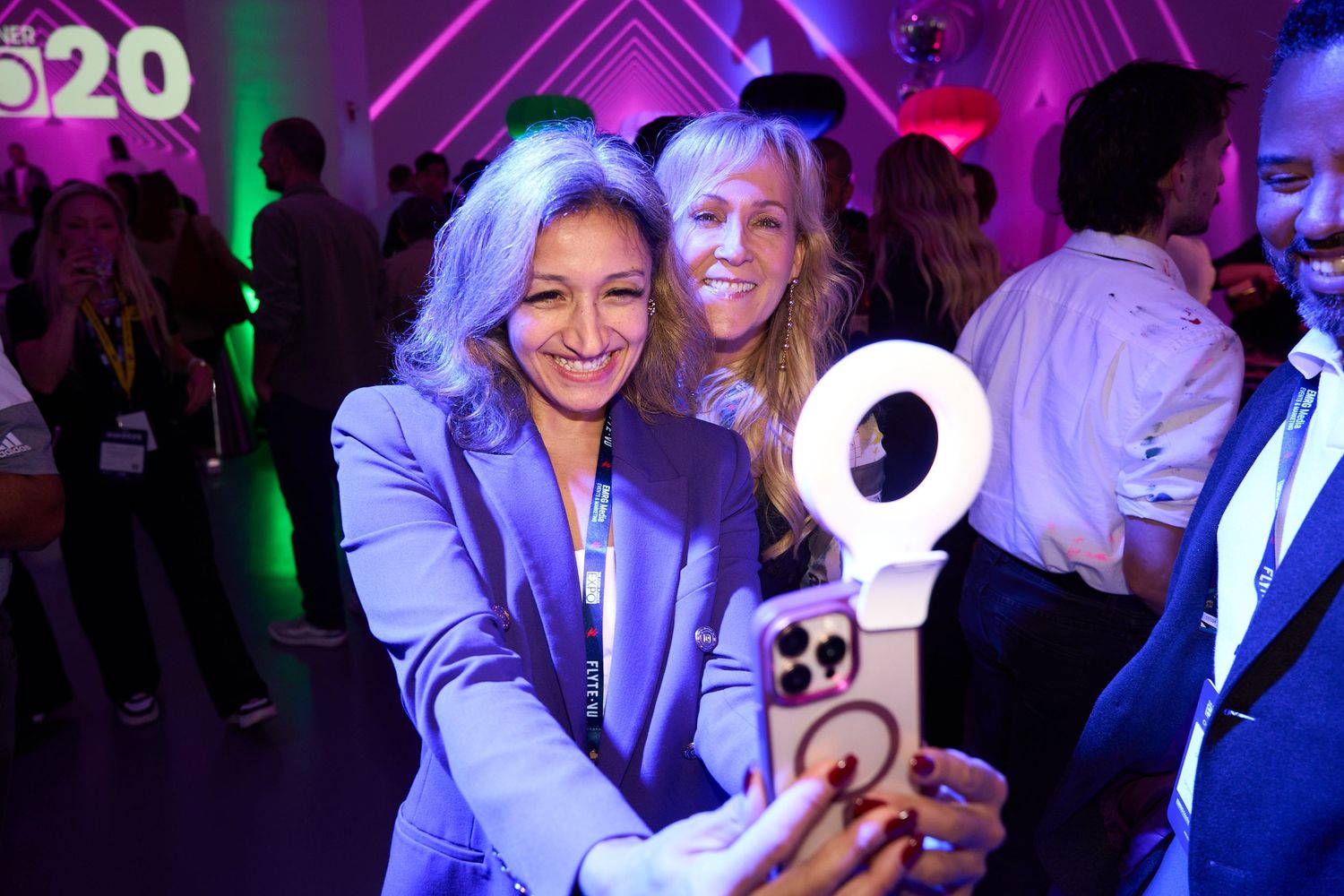People dancing and socializing at a nightclub with vibrant purple and green lighting effects.
