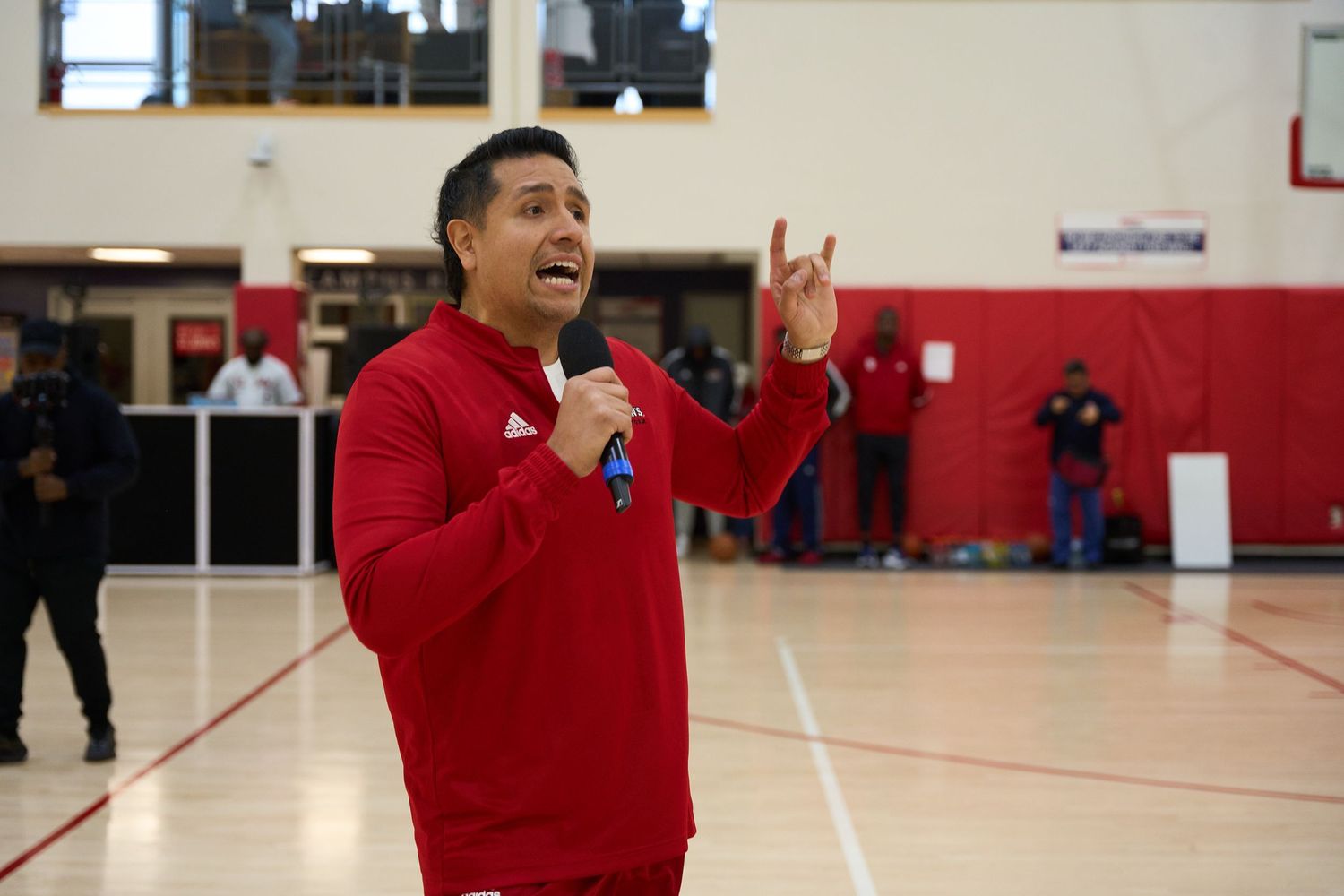 Indoor gymnasium with red walls and basketball hoops visible in the background.