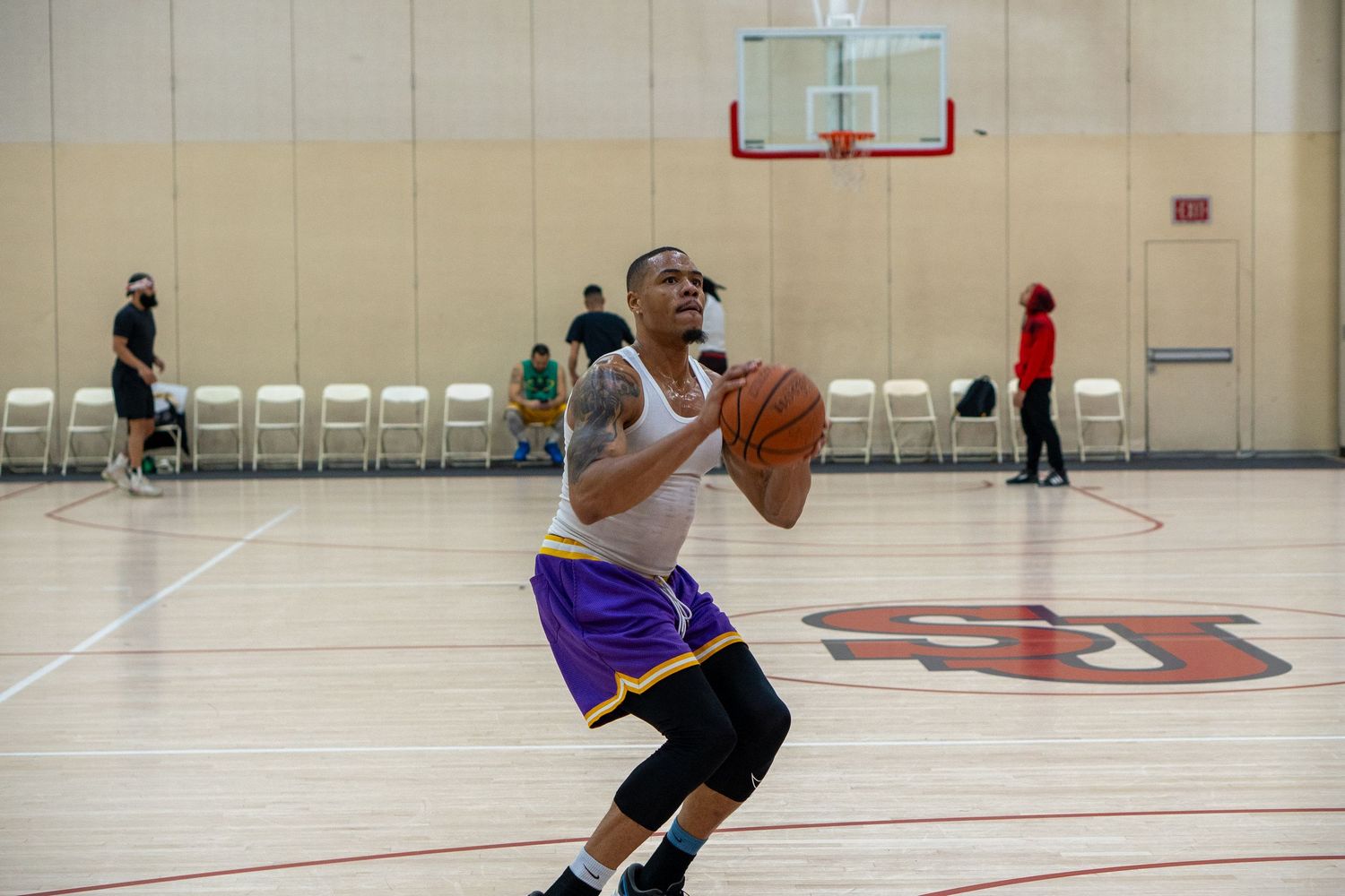 Basketball players practice shooting drills and dribbling exercises in a gymnasium during a training session.