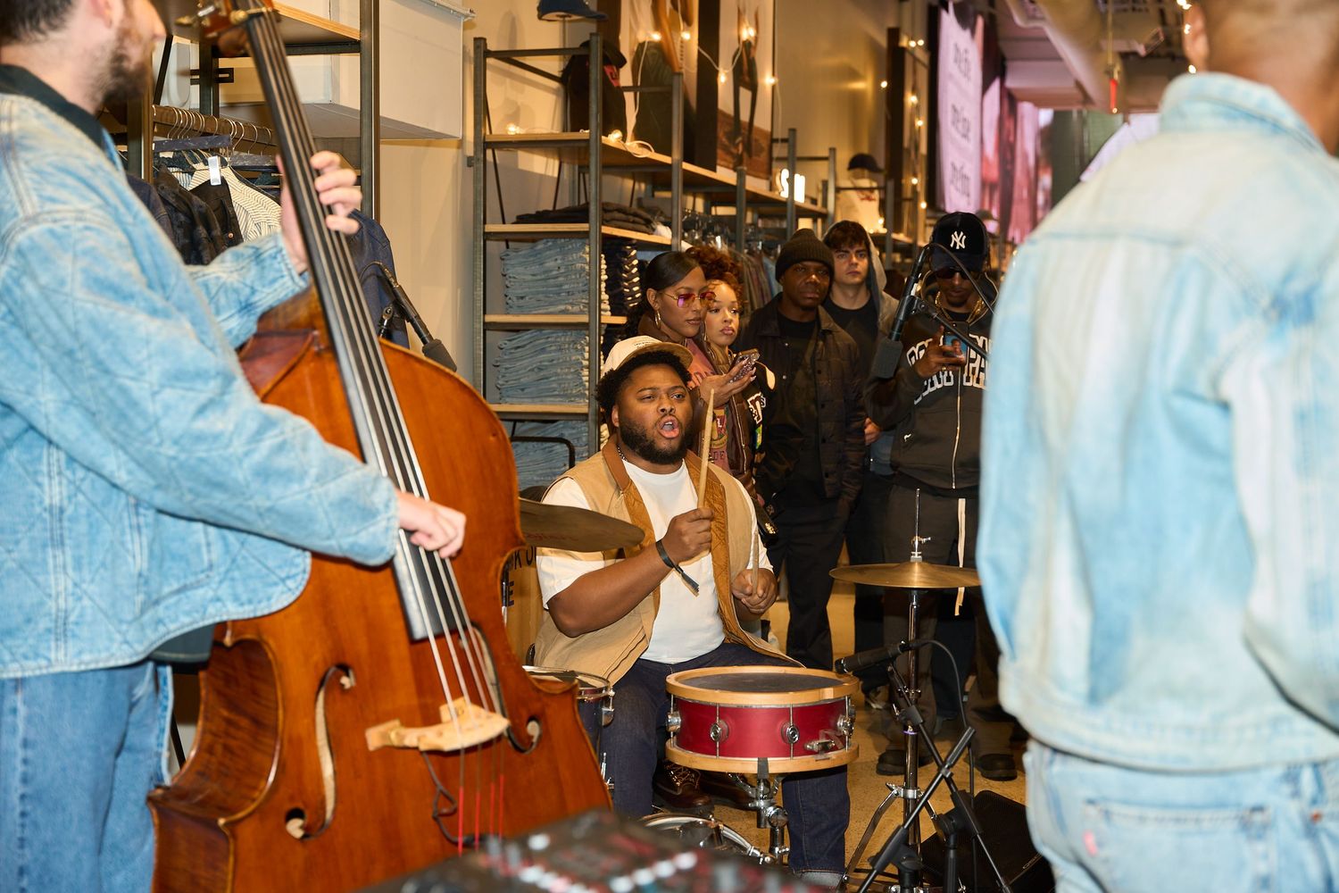 Musicians performing in a crowded indoor space with instruments including drums and bass.