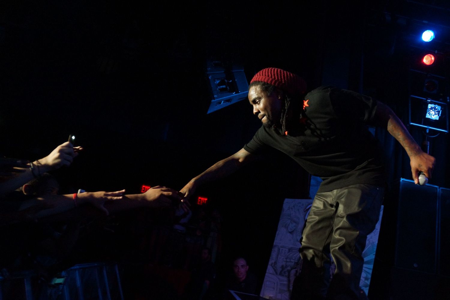 A performer in a red beanie leans forward towards the crowd during a nighttime concert performance.