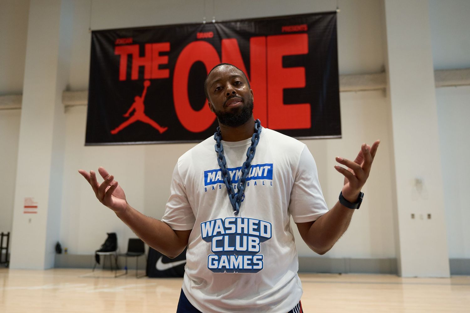 Person in white t-shirt gestures under red Jordan brand banner reading 'THE ONE' at basketball event.