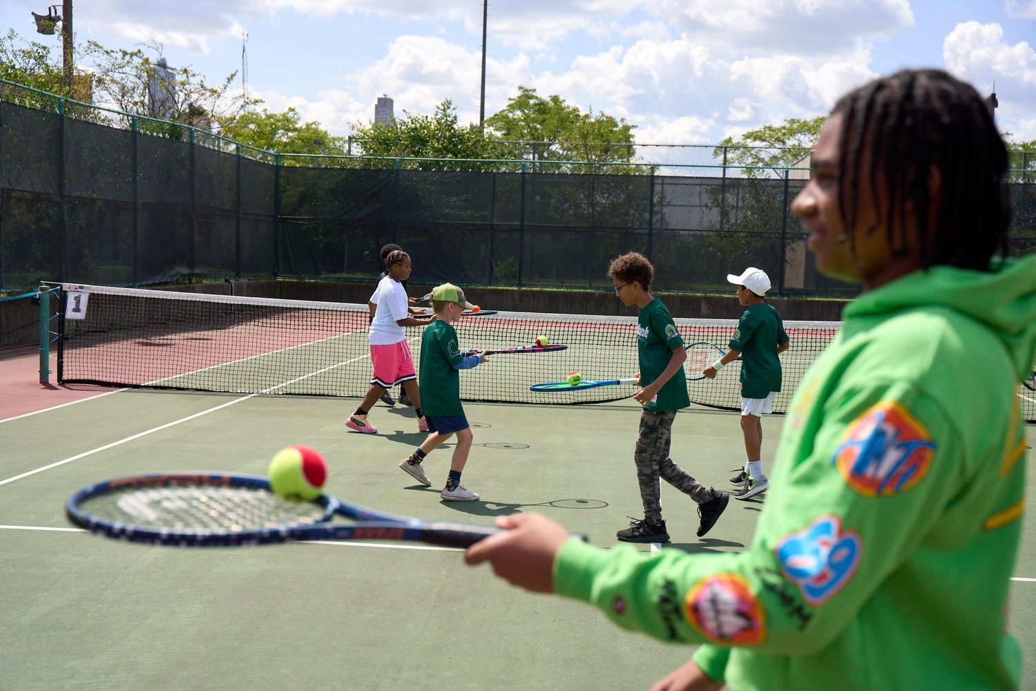 Players practicing tennis drills and techniques on multiple outdoor courts during a training session.