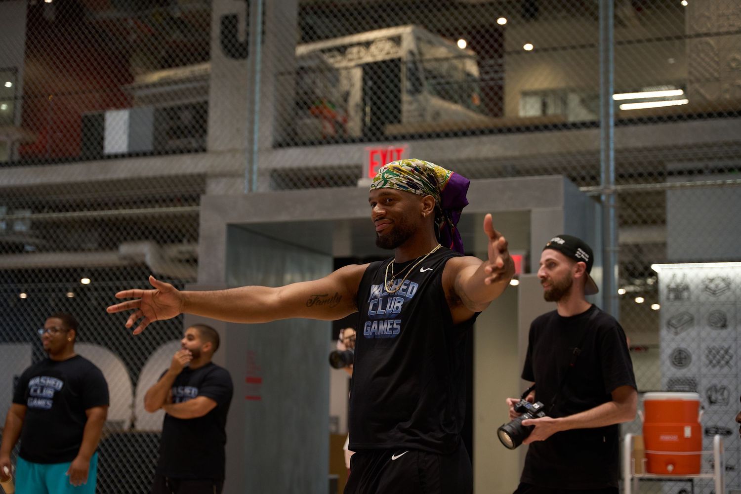 Athletes in black shirts stretch and warm up together in a large indoor fitness space during group exercise training.