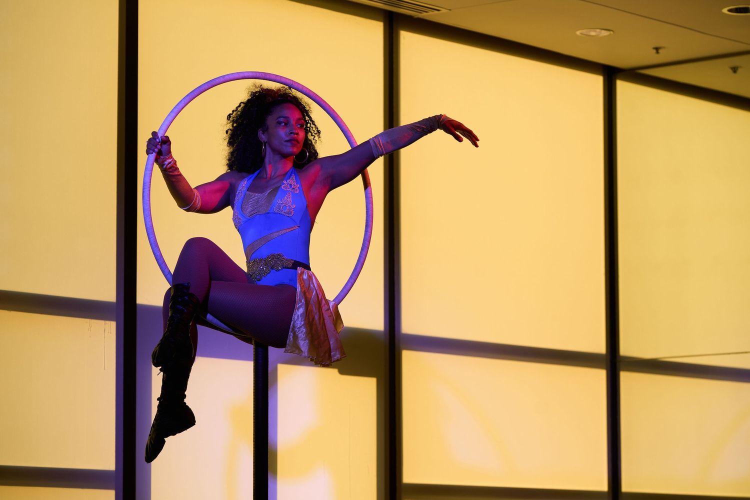 Silhouetted performer balances gracefully in a circular hoop against warm yellow backlighting with blue accent lighting.