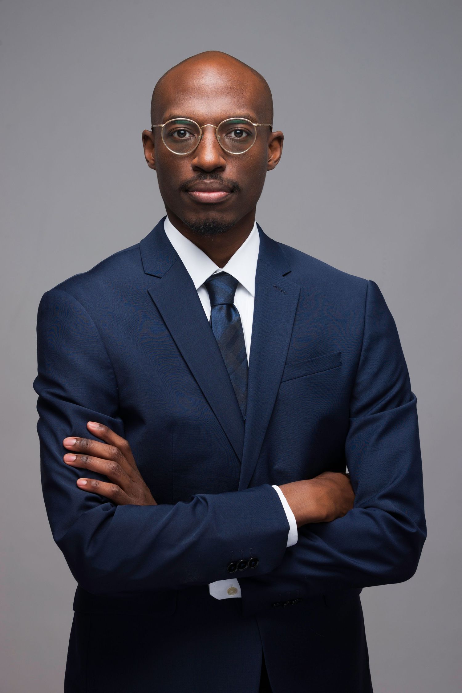 Professional portrait series showing a person in a navy suit and tie with glasses against a gray background in various poses.