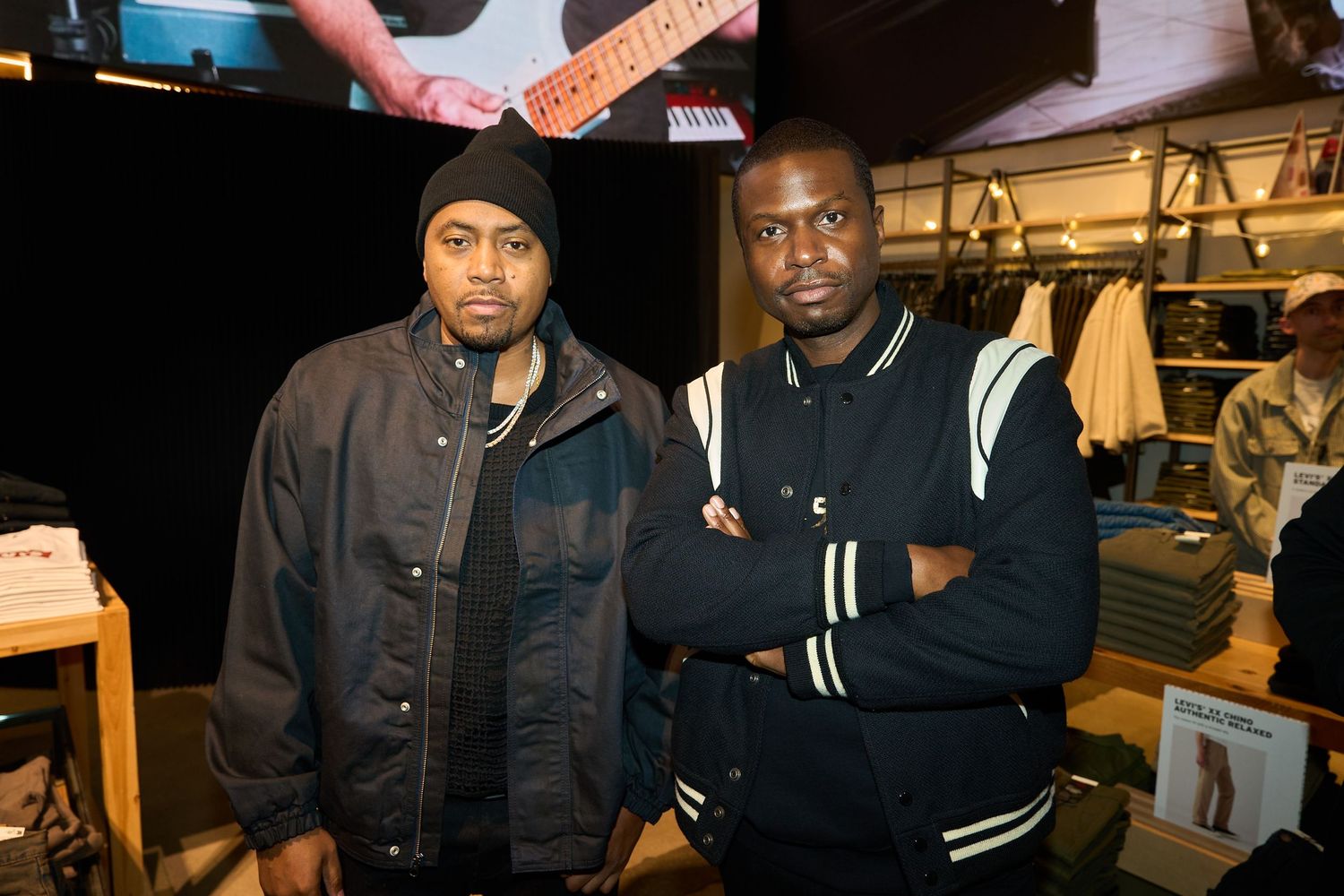 Two performers in dark jackets stand together backstage at a music venue during a show.