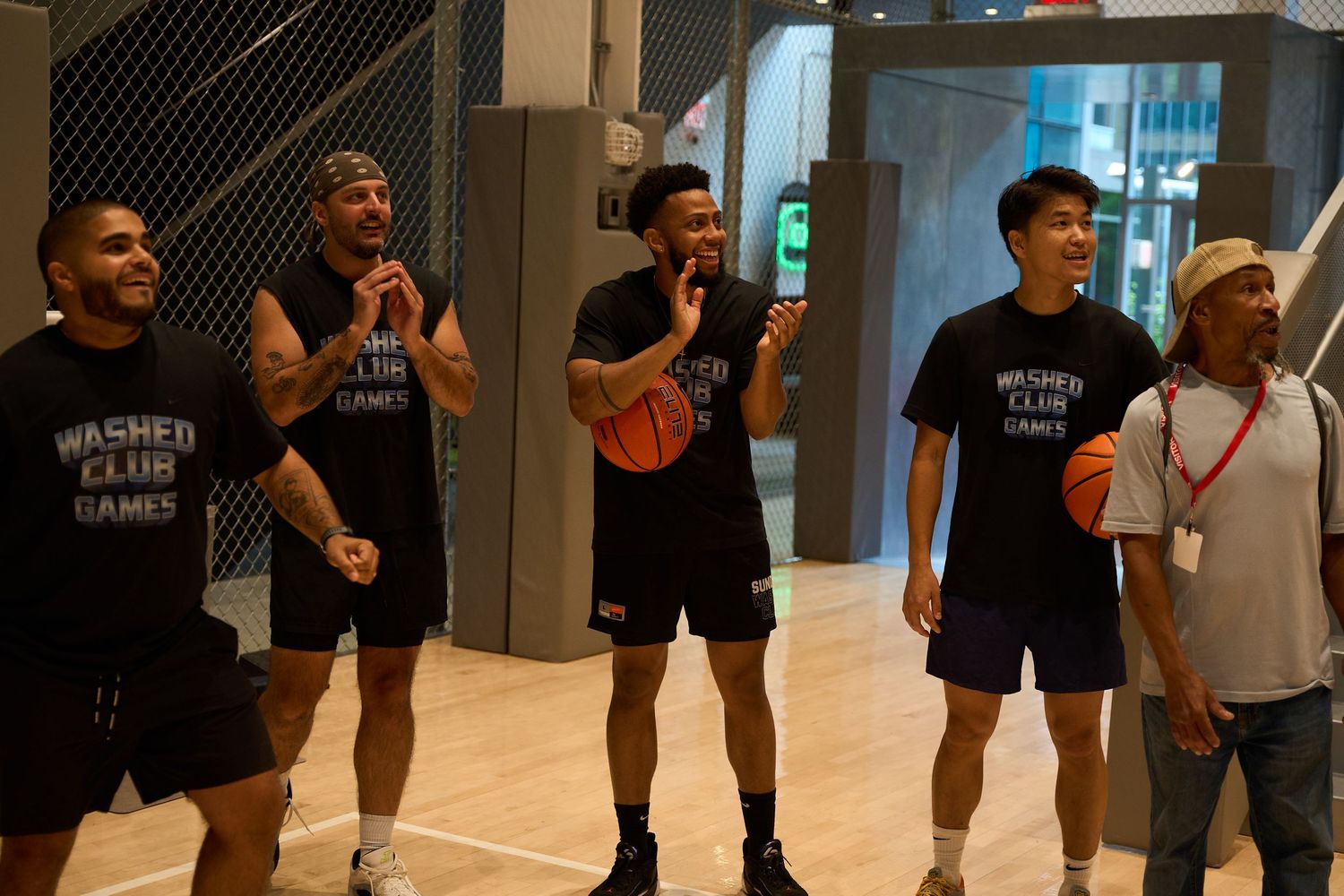 Basketball players in black t-shirts gather on an indoor court for practice or training session.