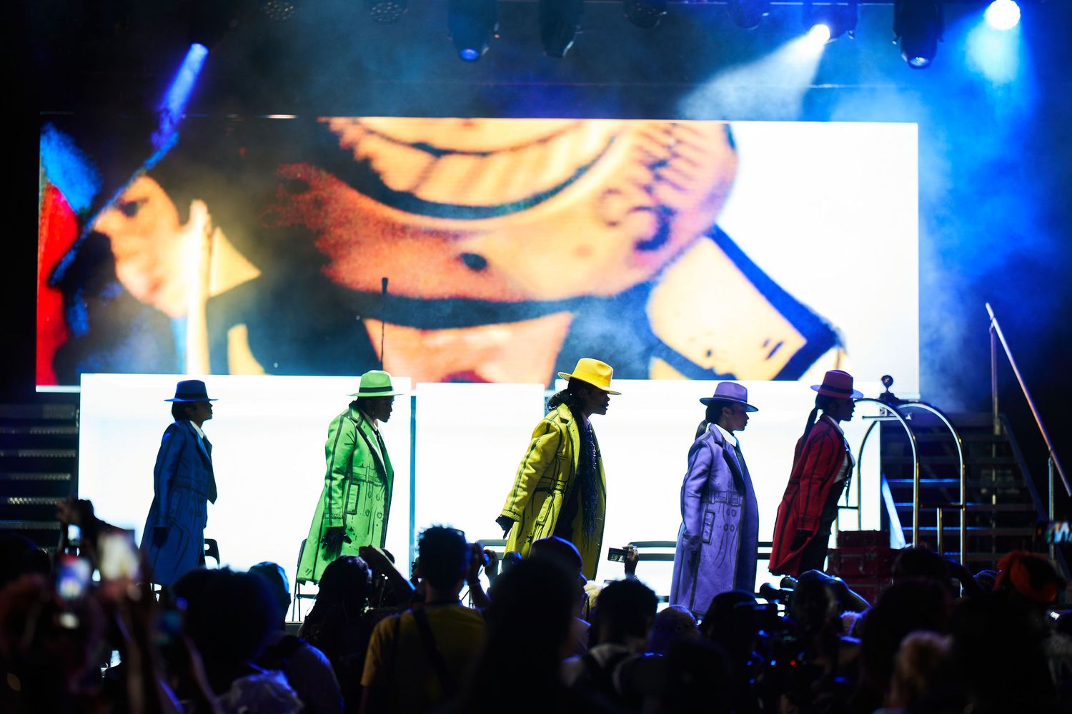 Blue stage lighting illuminates silhouetted performers against dark background during live concert performance.
