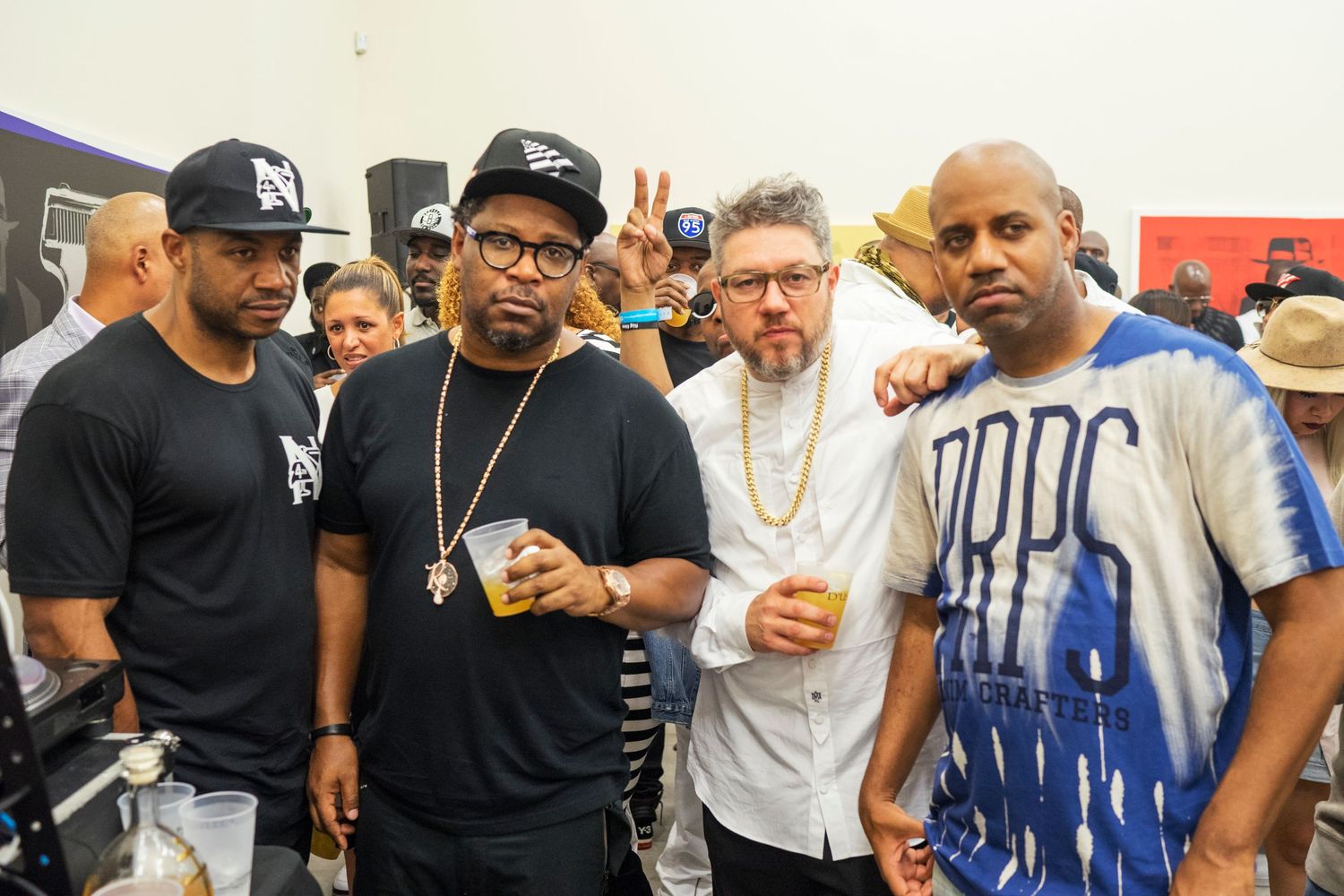 Four men pose together at an outdoor event, with two wearing casual black shirts and one in a blue and white outfit.