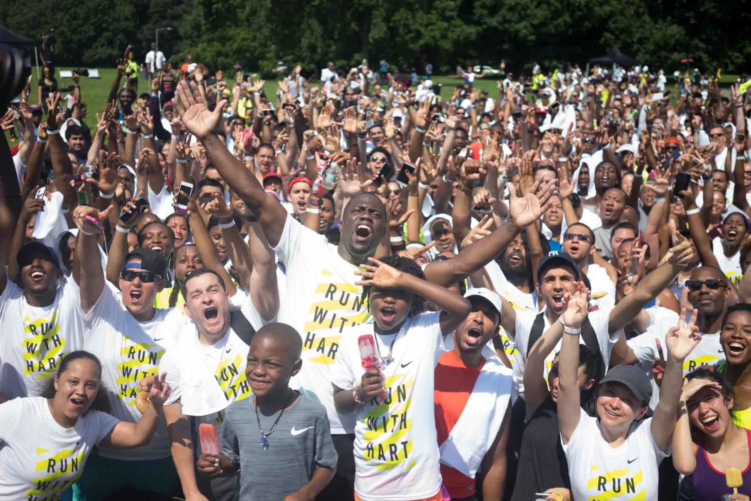 Large crowd of marathon runners cheering and raising their arms at an outdoor racing event.