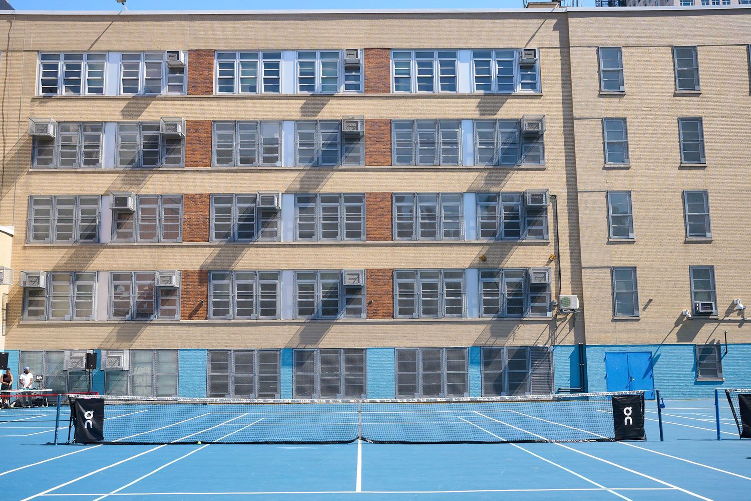 Blue tennis courts with white lines surrounded by residential buildings on a sunny day.