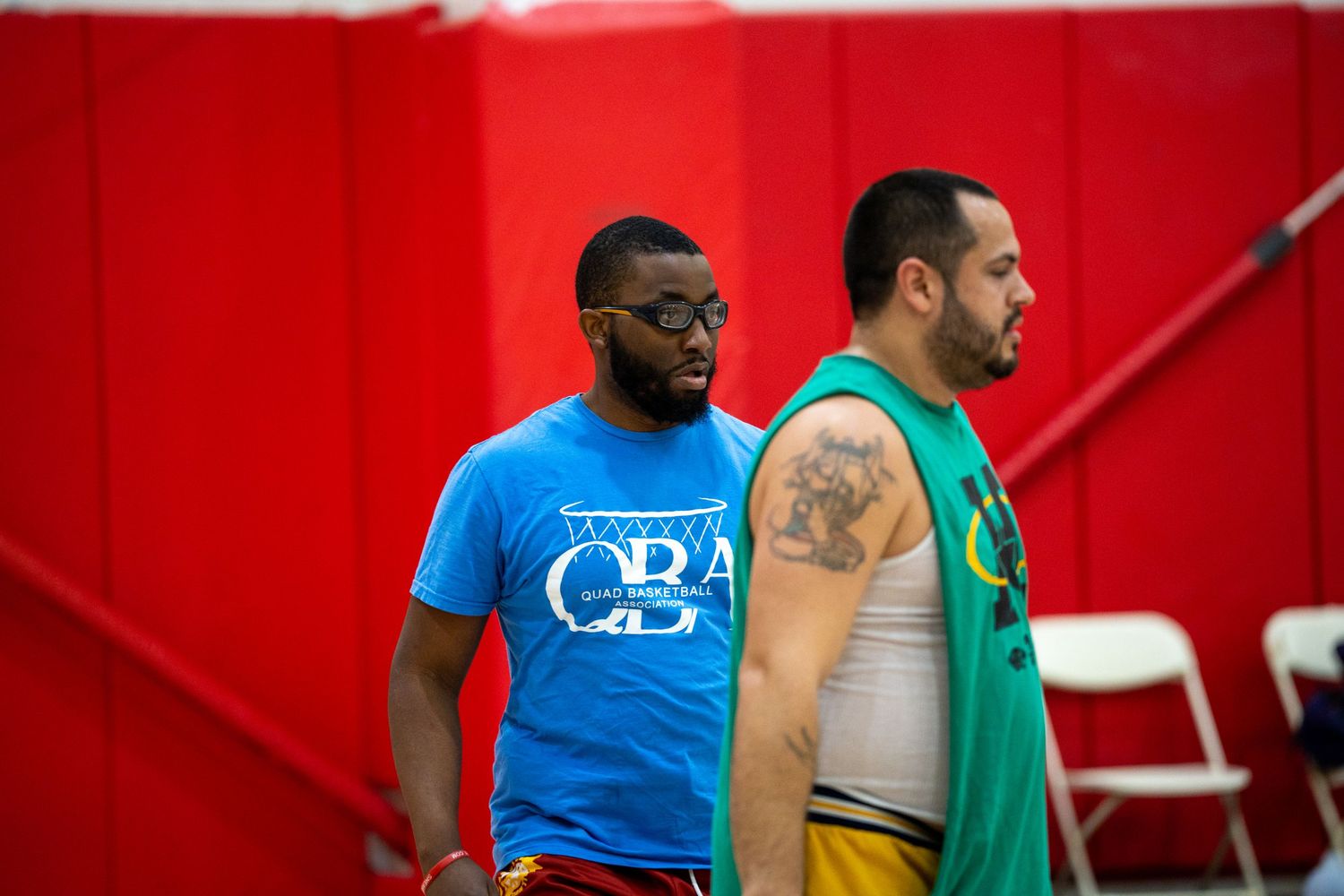 Athletes in blue and green shirts participate in a sports training session in a red-walled facility.